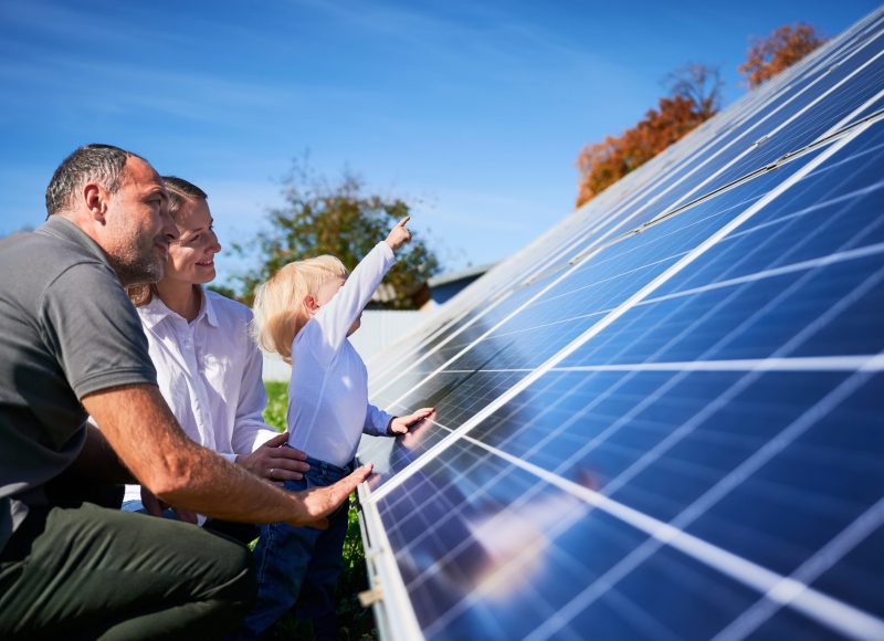Enthusiastic father showing potential of alternative energy. Contemporary family looking at new solar panels they bought. Side view of happy parents and interested child next to solar panels.